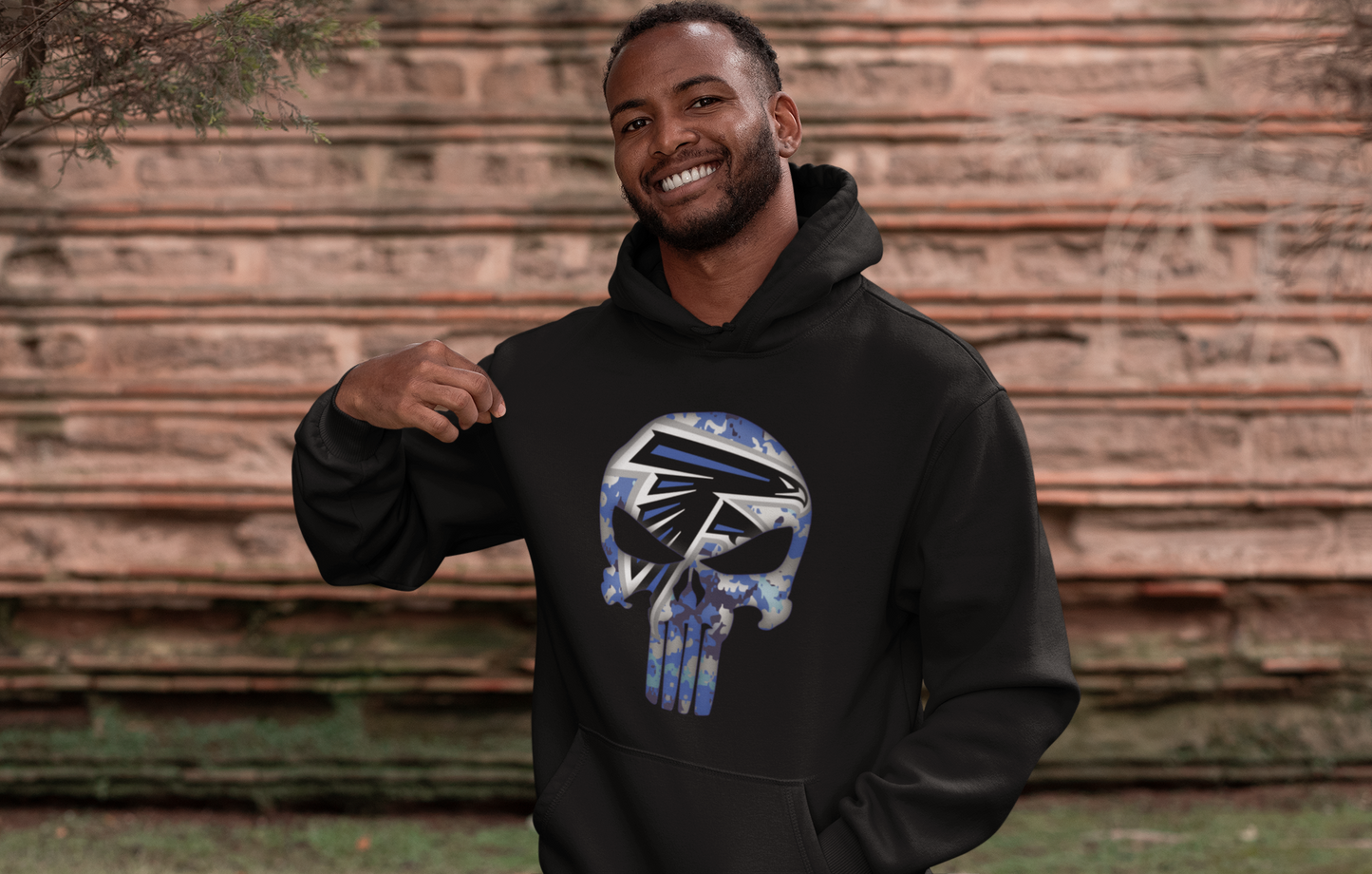 Smiling man wearing a black adult unisex sponge fleece pullover hooded sweatshirt with Sharon Springs Falcons “Punisher" logo and pointing to logo on sweatshirt